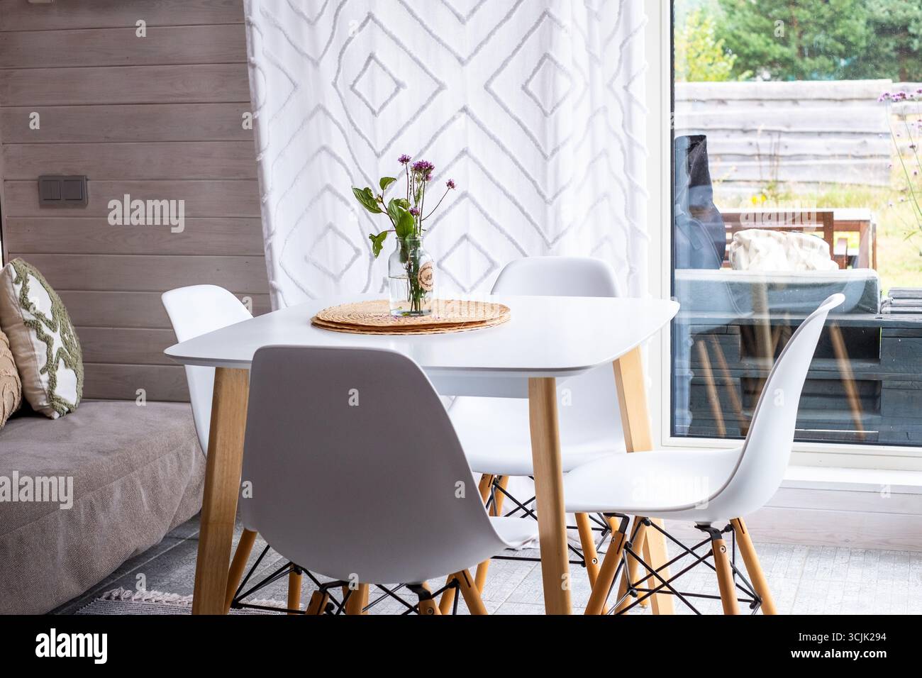 La luminosa zona pranzo scandinava presenta un design minimalista con sedie bianche e tavolo in legno, creando un'atmosfera intima piena di luce naturale Foto Stock