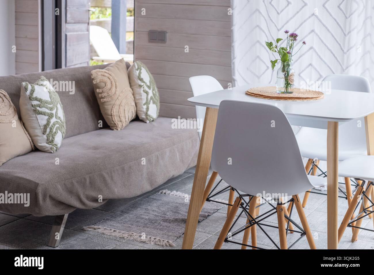 Gli interni scandinavi presentano un divano minimalista decorato con cuscini, un luminoso tavolo da pranzo e un ambiente intimo, che enfatizza il design funzionale e Foto Stock