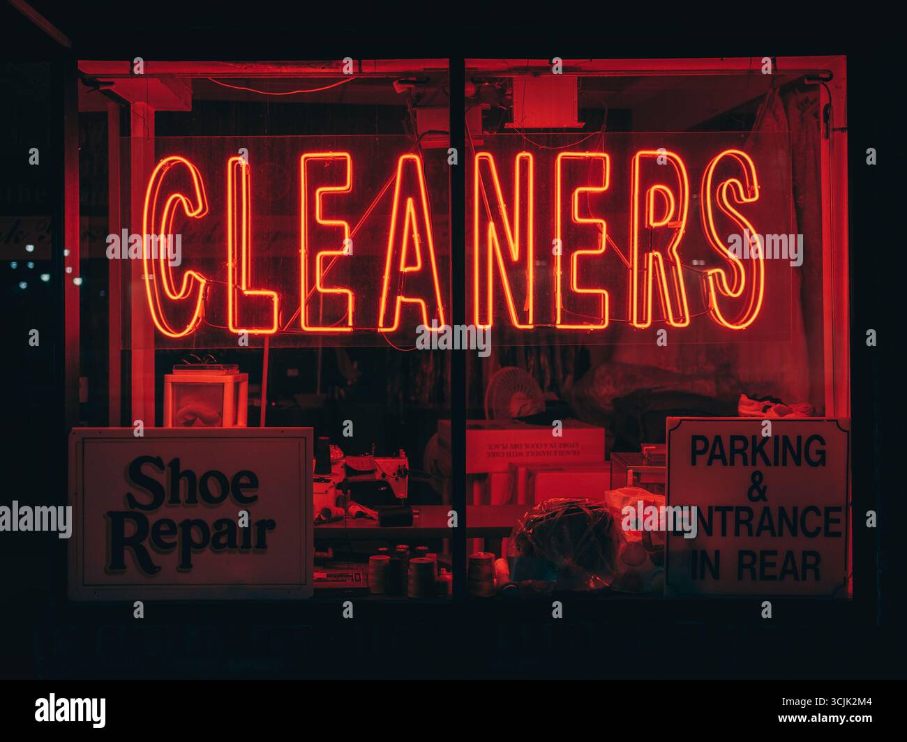 Una vetrina mostra i cartelli al neon per i pulitori e i cartelli per la riparazione delle scarpe e il parcheggio sul retro di New York City Foto Stock