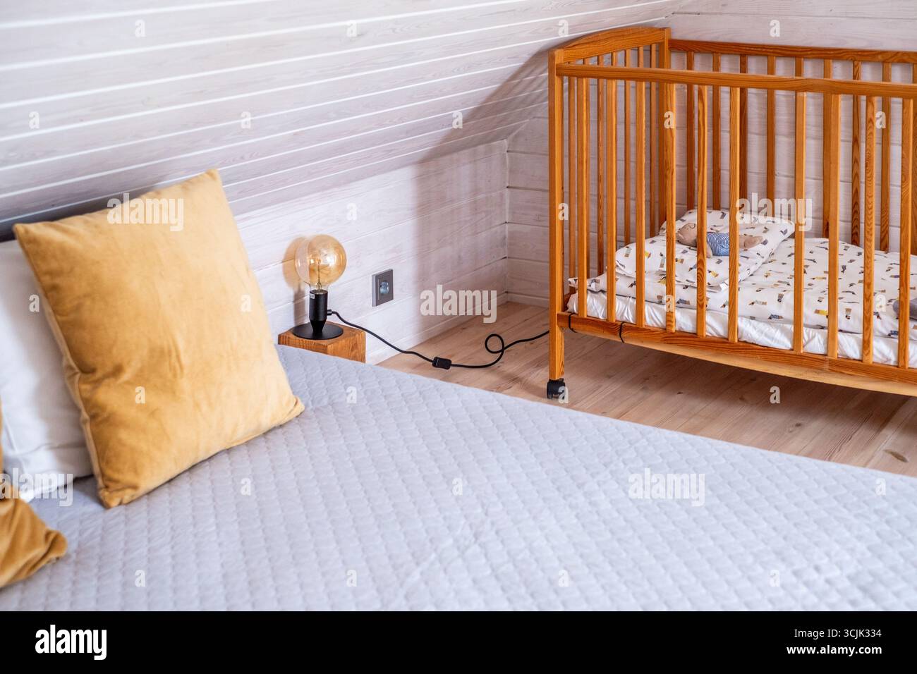 La camera da letto in stile scandinavo presenta un'accogliente culla accanto a un morbido letto, una calda illuminazione e toni neutri, creando uno spazio luminoso e invitante con copie Foto Stock