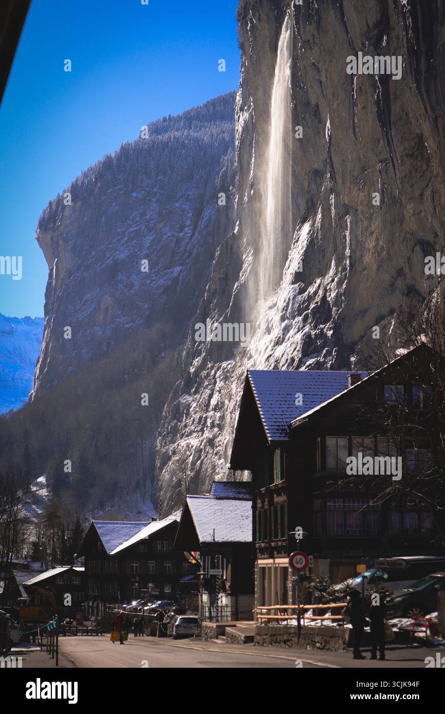 Case svizzere innevate durante l'inverno con vista sulle cascate di montagna sullo sfondo nei dintorni di Interlaken in Svizzera Foto Stock