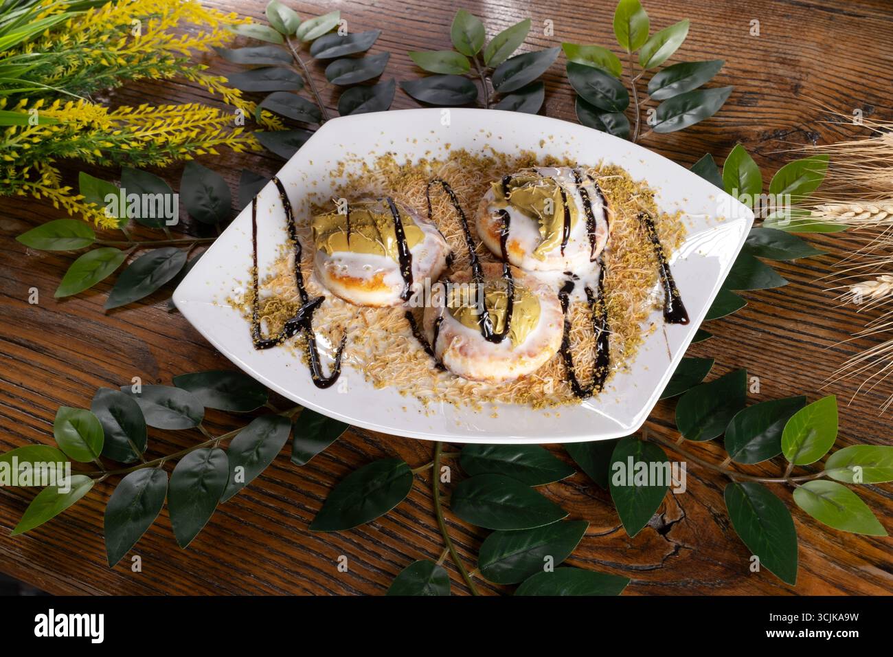 Una foto di Sirniki, un dessert ucraino, servito con pistacchio, salsa al cioccolato, gelato, e kadayif, che offre una delizia deliziosa e appagante. Foto Stock