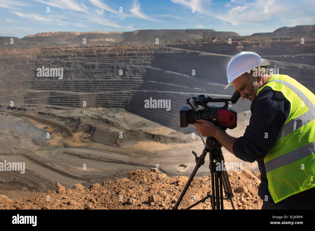 cameraman che gestisce una fotocamera su un treppiede, in una miniera a cielo aperto che realizza un documentario Foto Stock