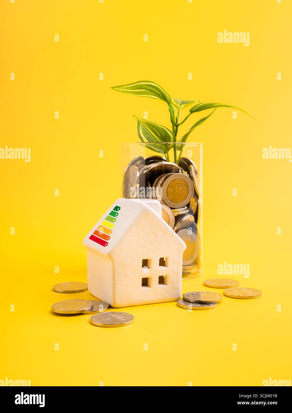 Modello di casa a risparmio energetico con etichetta di classificazione ecologica accanto al vaso di monete e piante verdi, simbolo del risparmio energetico, della vita sostenibile, della crescita finanziaria Foto Stock