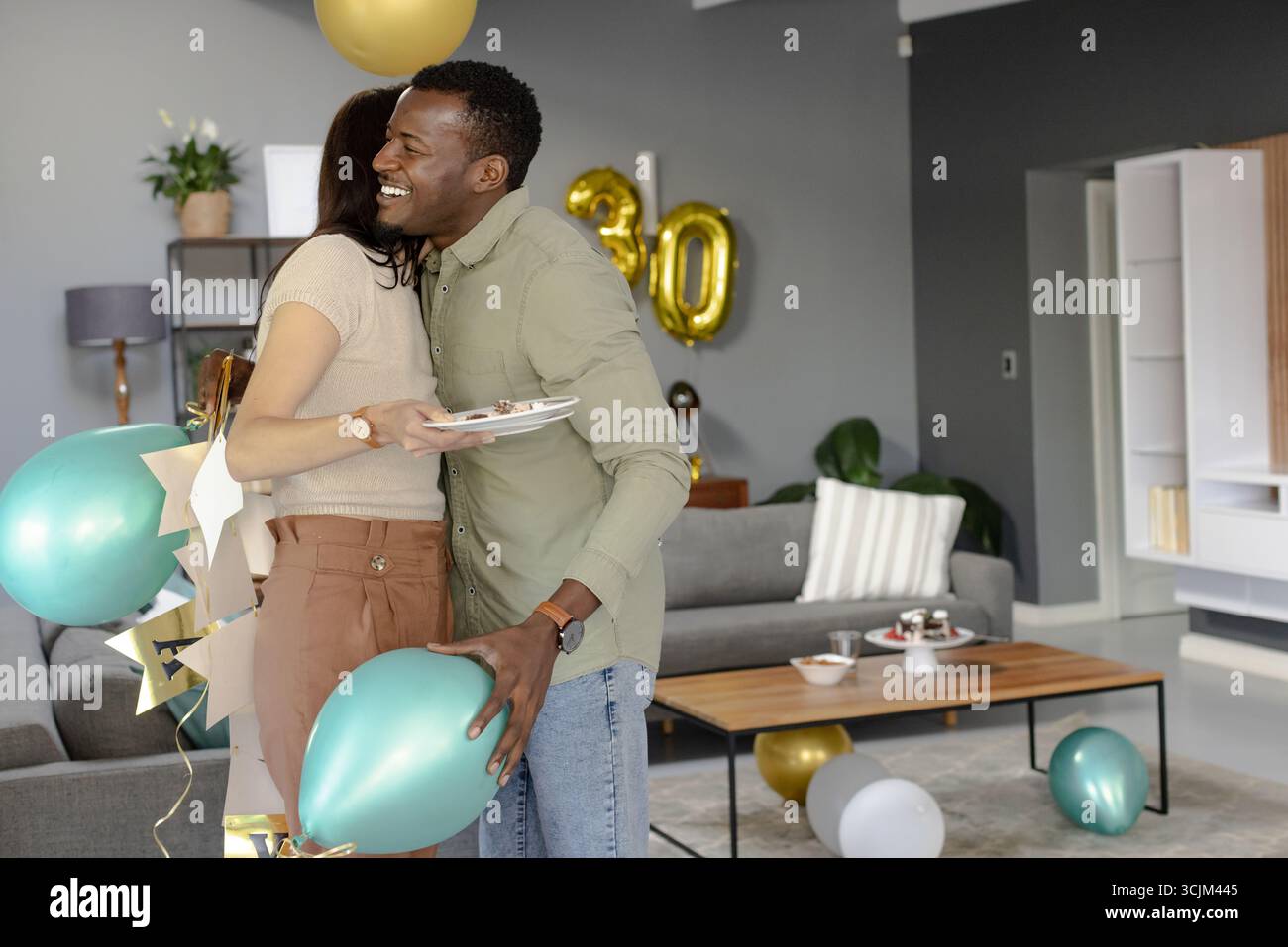 Amici che abbracciano e festeggiano il compleanno con palloncini e torta a casa Foto Stock