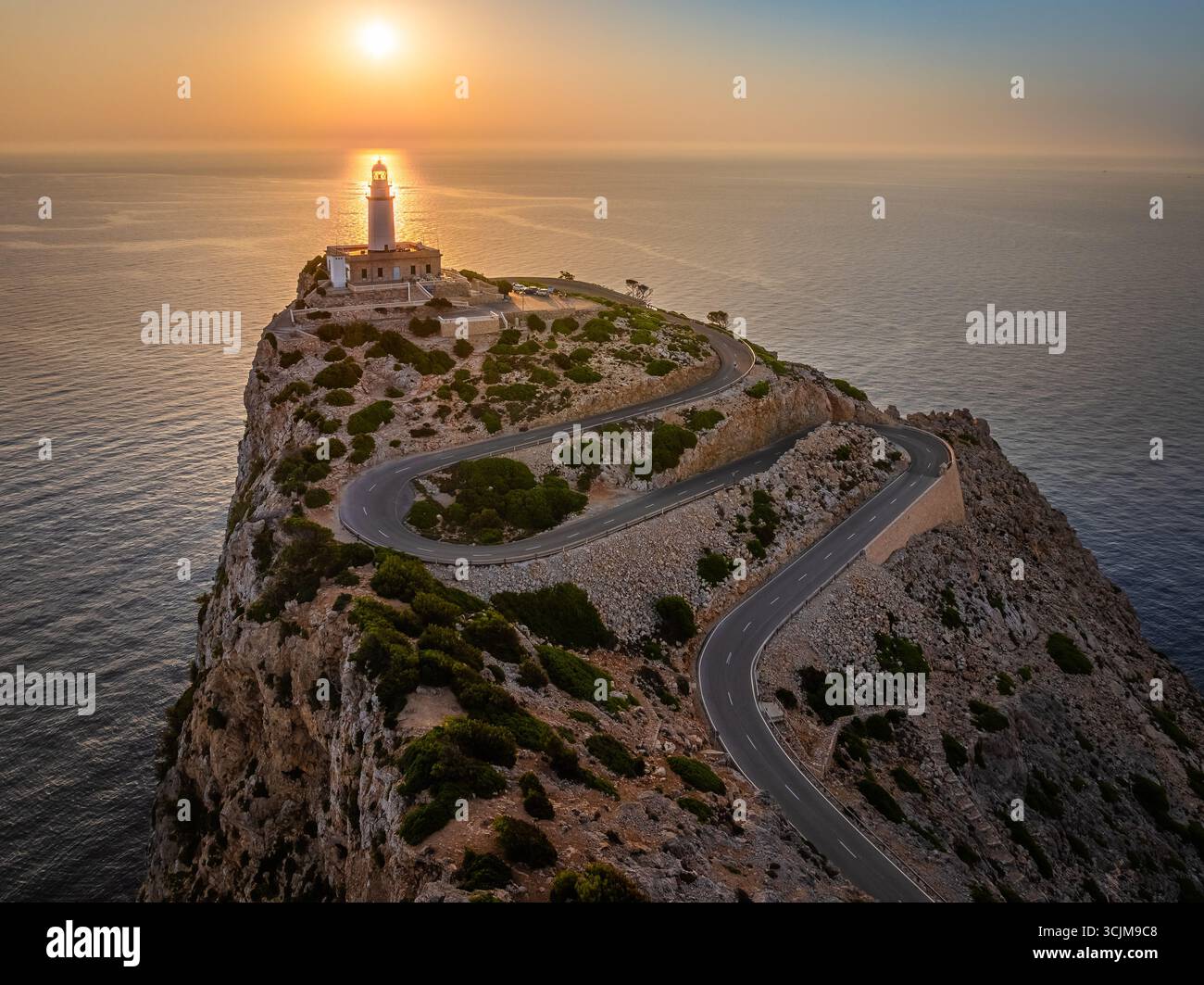 Maiorca, Spagna - Vista aerea del faro e della strada a serpentina a Cap de Formentor all'alba con luce calda, nuvole e cielo blu Foto Stock