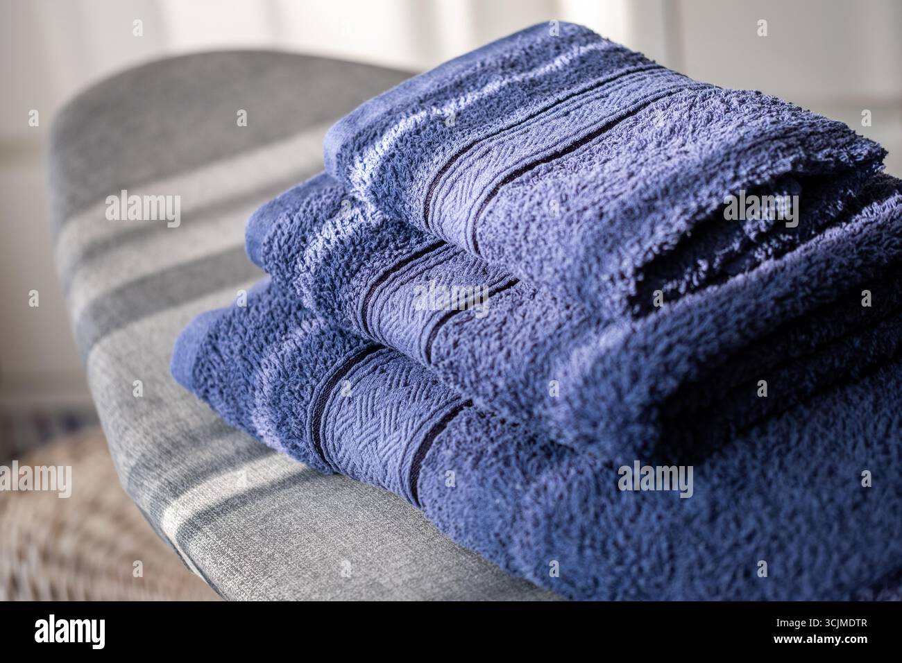 I morbidi asciugamani blu sono disposti in modo ordinato su un asse da stiro, evidenziando il loro aspetto fresco e ordinato, contribuendo a creare un ambiente accogliente e organizzato Foto Stock