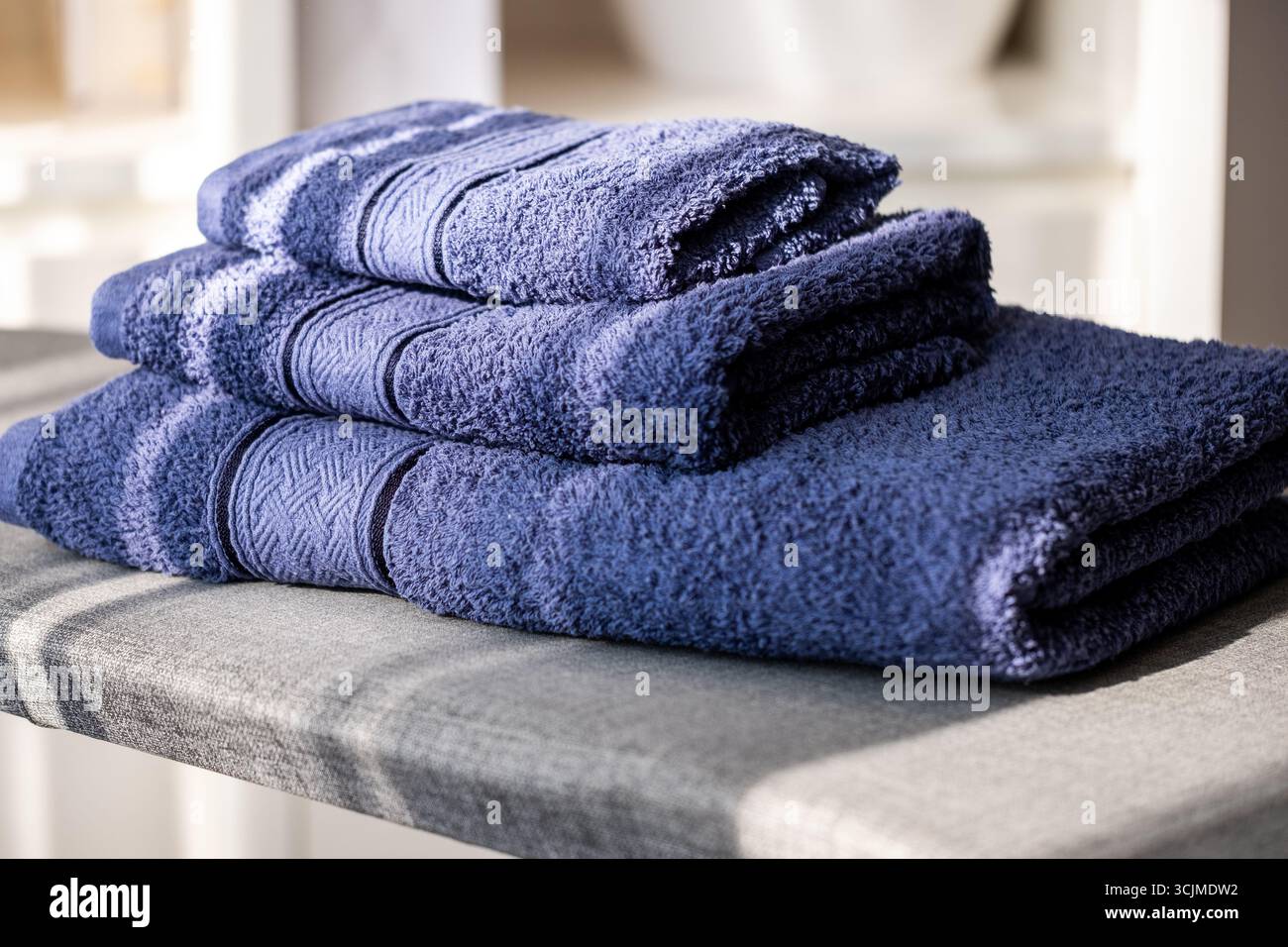 I morbidi asciugamani blu navy sono ben piegati e impilati su una superficie ruvida, creando un'atmosfera organizzata e accogliente in un bagno fresco Foto Stock