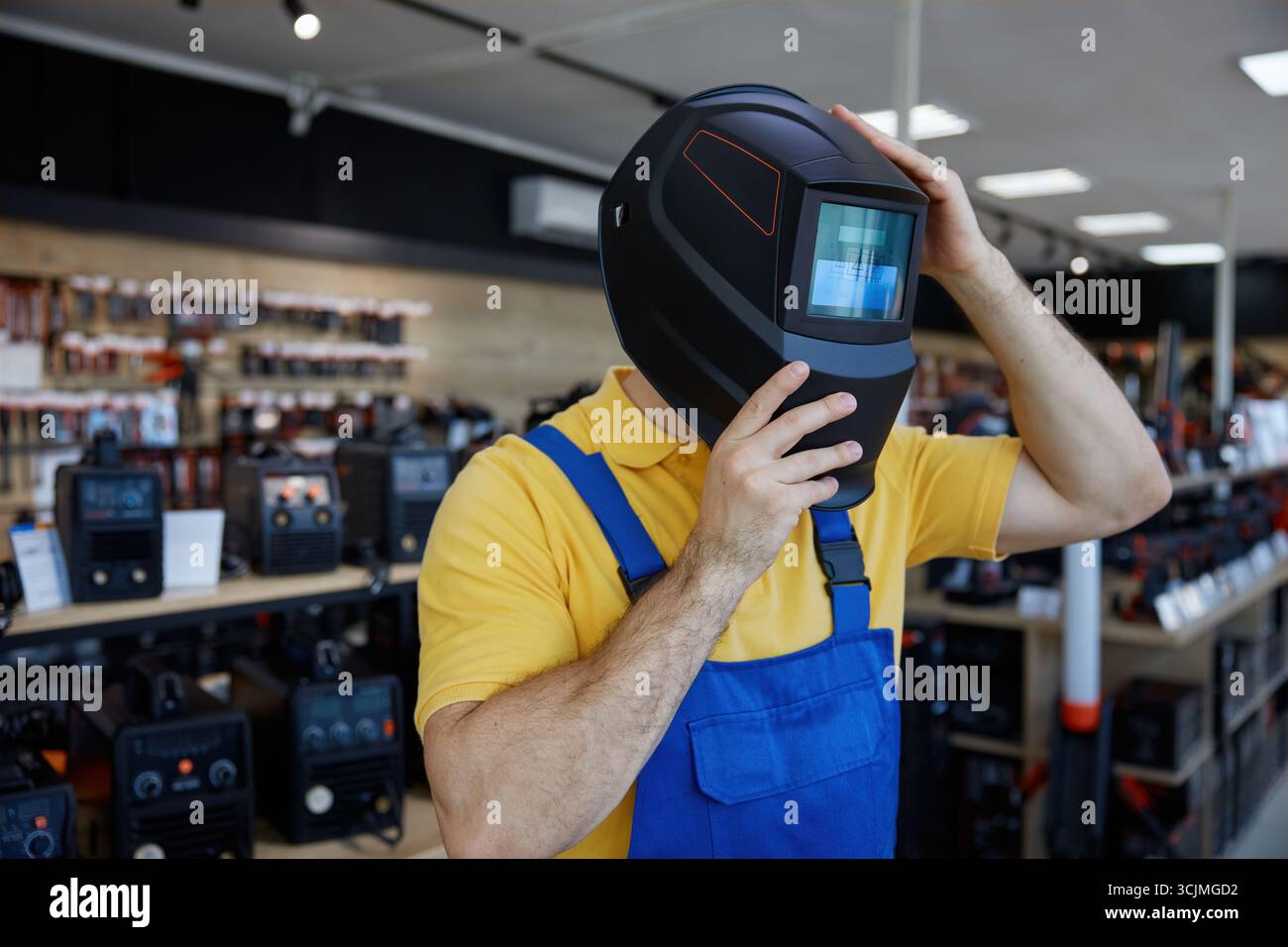 Uomo in un abbigliamento da lavoro che indossa un casco protettivo per saldatura all'interno di un negozio Foto Stock
