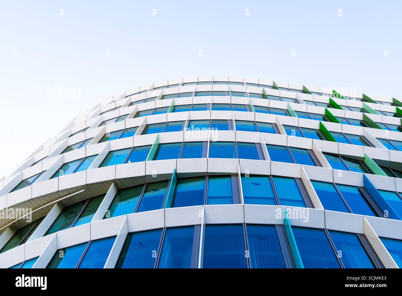 Facciata colorata di un edificio di uffici con pannelli di finestre angolati in una disposizione geometrica verde, viola e blu. Foto Stock