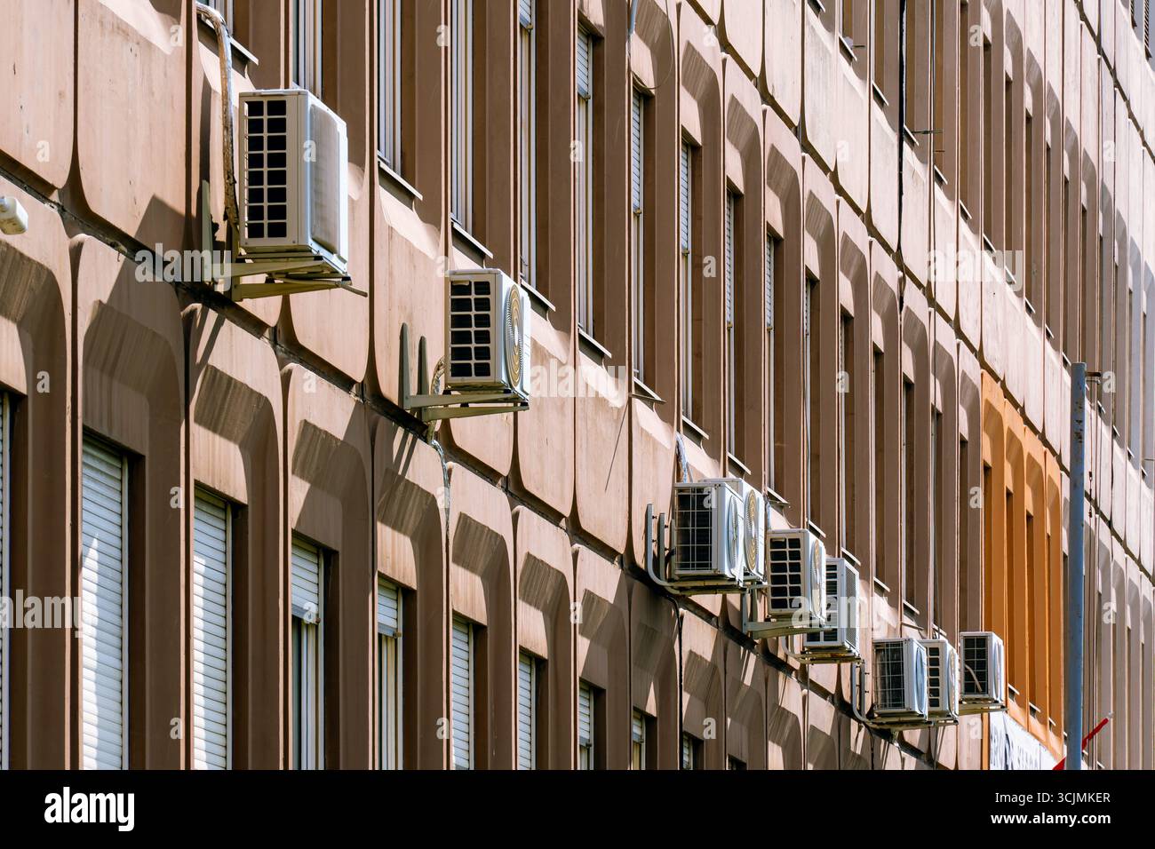 Facciata di un vecchio edificio di uffici con finestre ripetitive, pannelli arancioni invecchiati e unità di aria condizionata visibili. Foto Stock