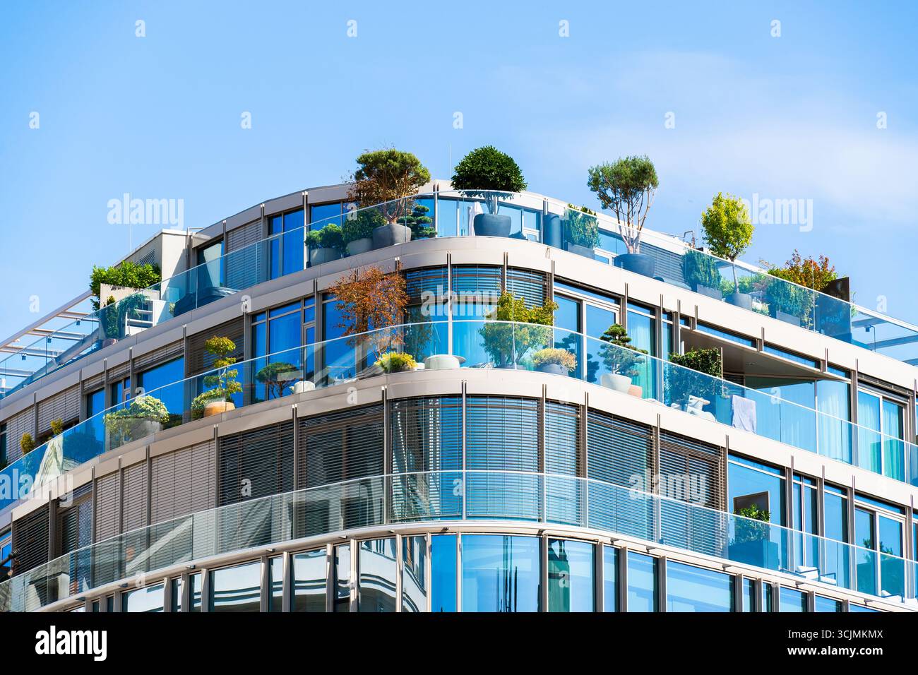 Moderno edificio per uffici con facciata in vetro e giardini sul tetto che mescolano architettura, sostenibilità e vegetazione urbana. Foto Stock