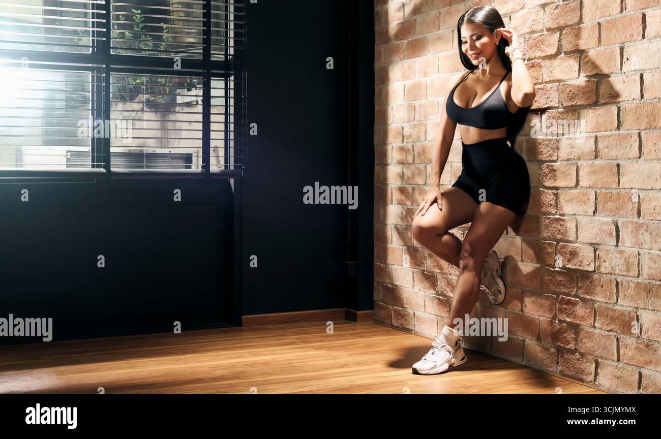 influencer del fitness che si appoggia contro il muro di mattoni allo studio fotografico Foto Stock