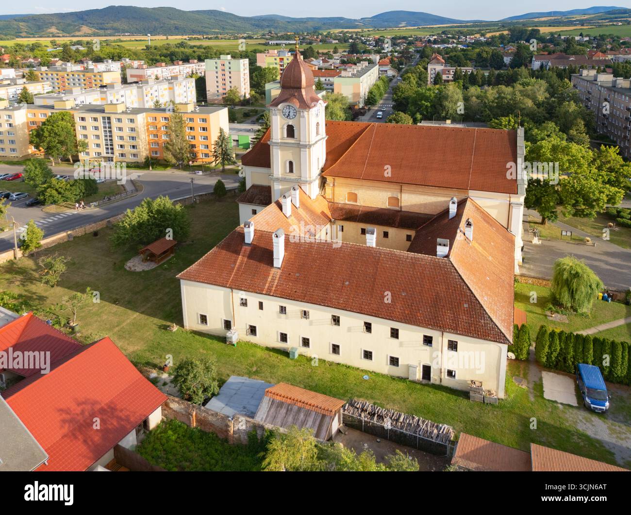 Vista aerea di una cattedrale storica con tetto piastrellato rosso, che getta lunghe ombre sugli edifici circostanti, Fiľakovo, regione di Banská Bystrica, Slovacchia. Foto Stock