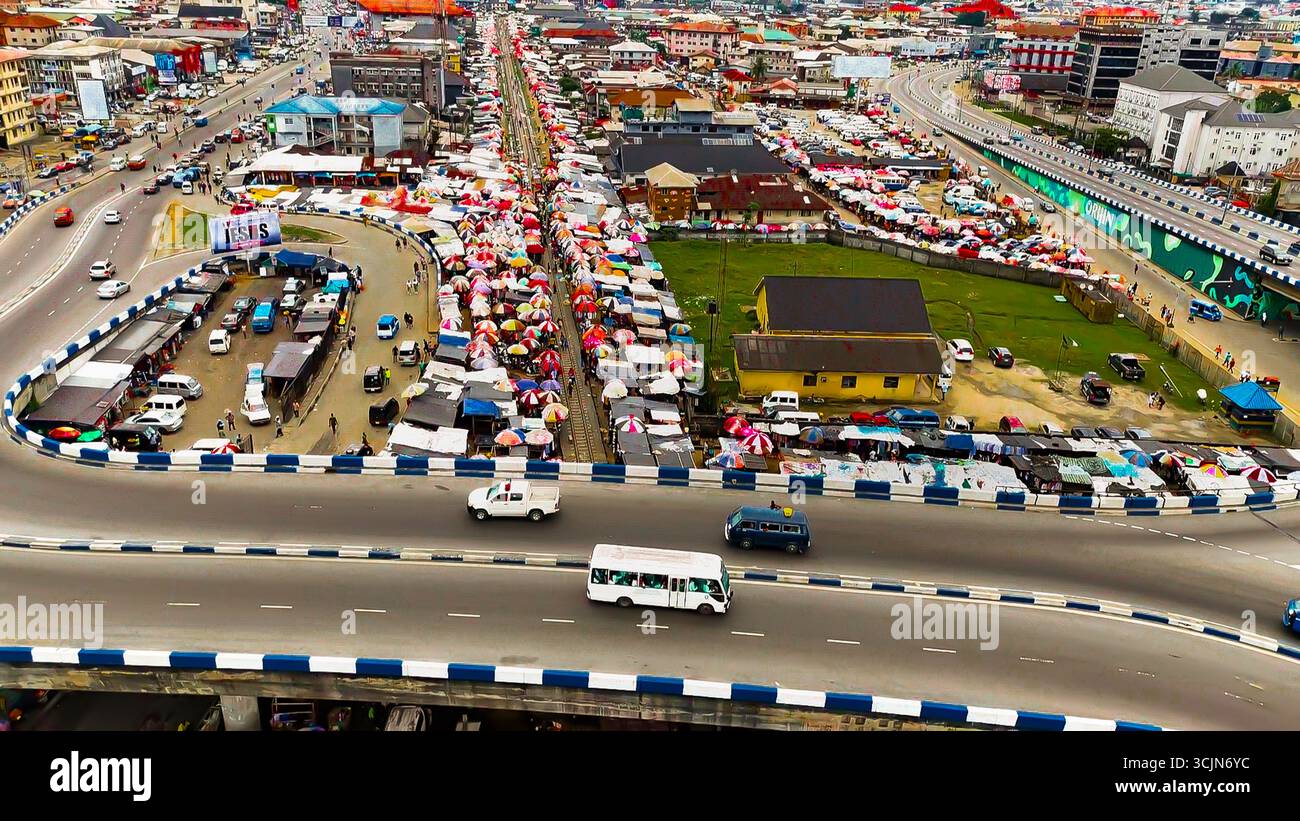 Vista aerea di una vivace strada del mercato brulicante di ombrelli colorati e venditori ambulanti, incorniciata dall'autostrada sopraelevata, dal parco Isaac boro, da Port Harcourt, Foto Stock
