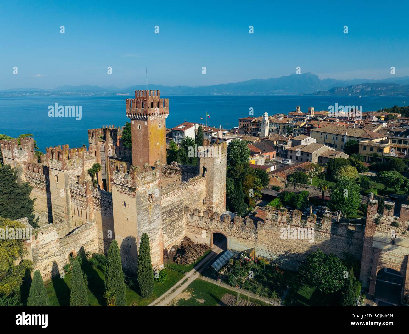 Vista aerea delle mura merlate del Castello Scaligero e della torre che si innalzano sopra l'antica città, con la distesa blu del Lago di Garda oltre, Lazise, Veneto, Italia. Foto Stock