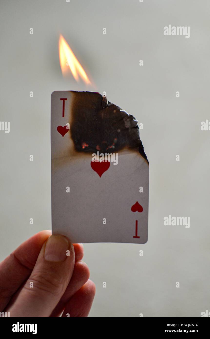 Una carta da gioco in mano, che è in fiamme, è stata incendiata. Foto Stock
