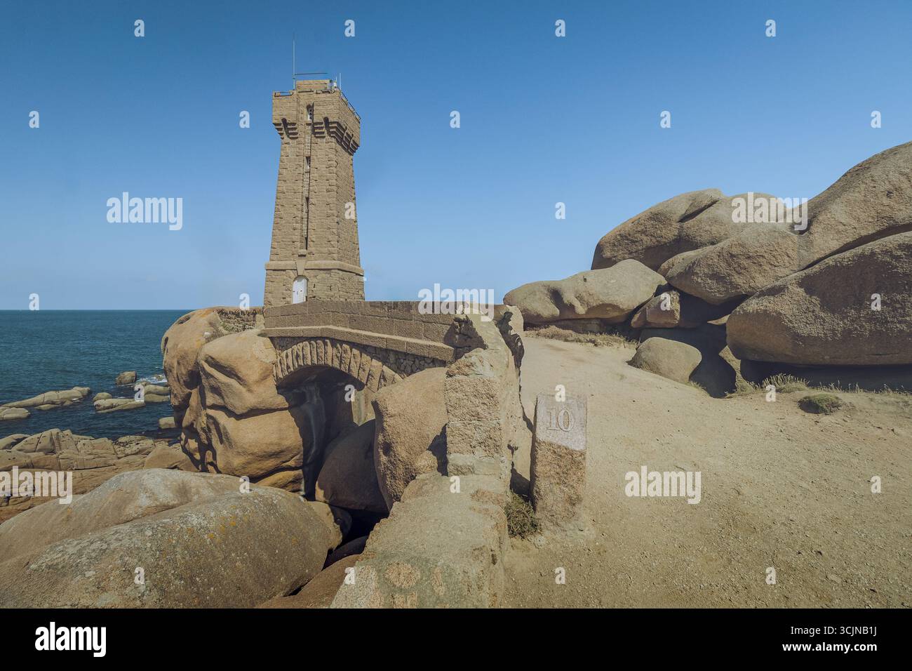 La vista del faro di Men Ruz si erge sull'aspra costa di granito rosa contro il cielo e il mare azzurri, Perros-Guirec, Bretagna, Francia. Foto Stock
