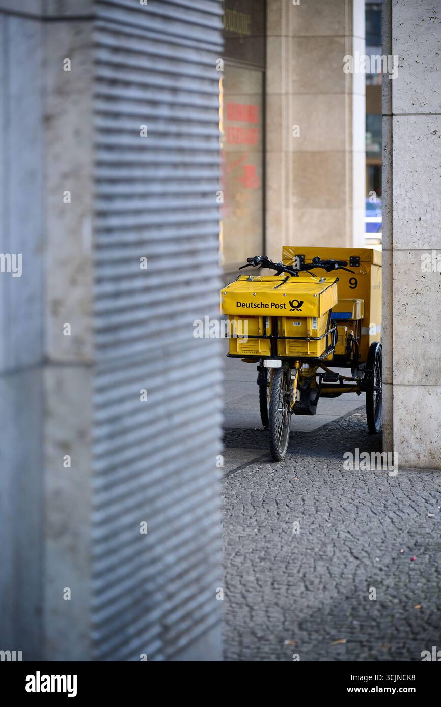 Carrello di consegna giallo parcheggiato da solo accanto a un muro di metallo in vicoli stretti, scatto verticale alla luce del giorno per logistica, servizi urbani ed editoriale industriale Foto Stock