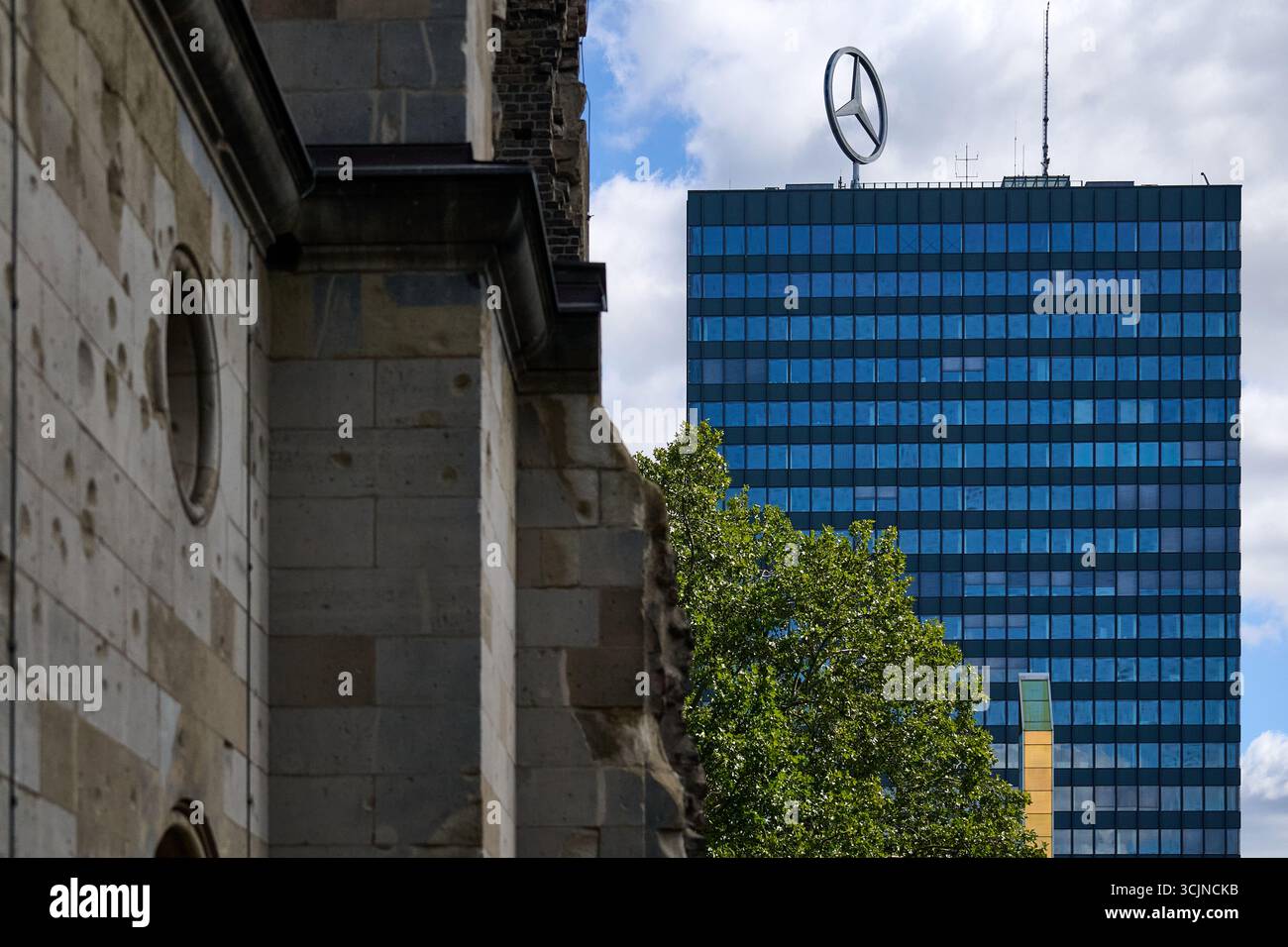 Logo Mercedes in cima alla moderna torre blu per uffici circondata da una storica chiesa in pietra alla luce del giorno, paesaggio urbano verticale per affari, contrasto e architettura Foto Stock