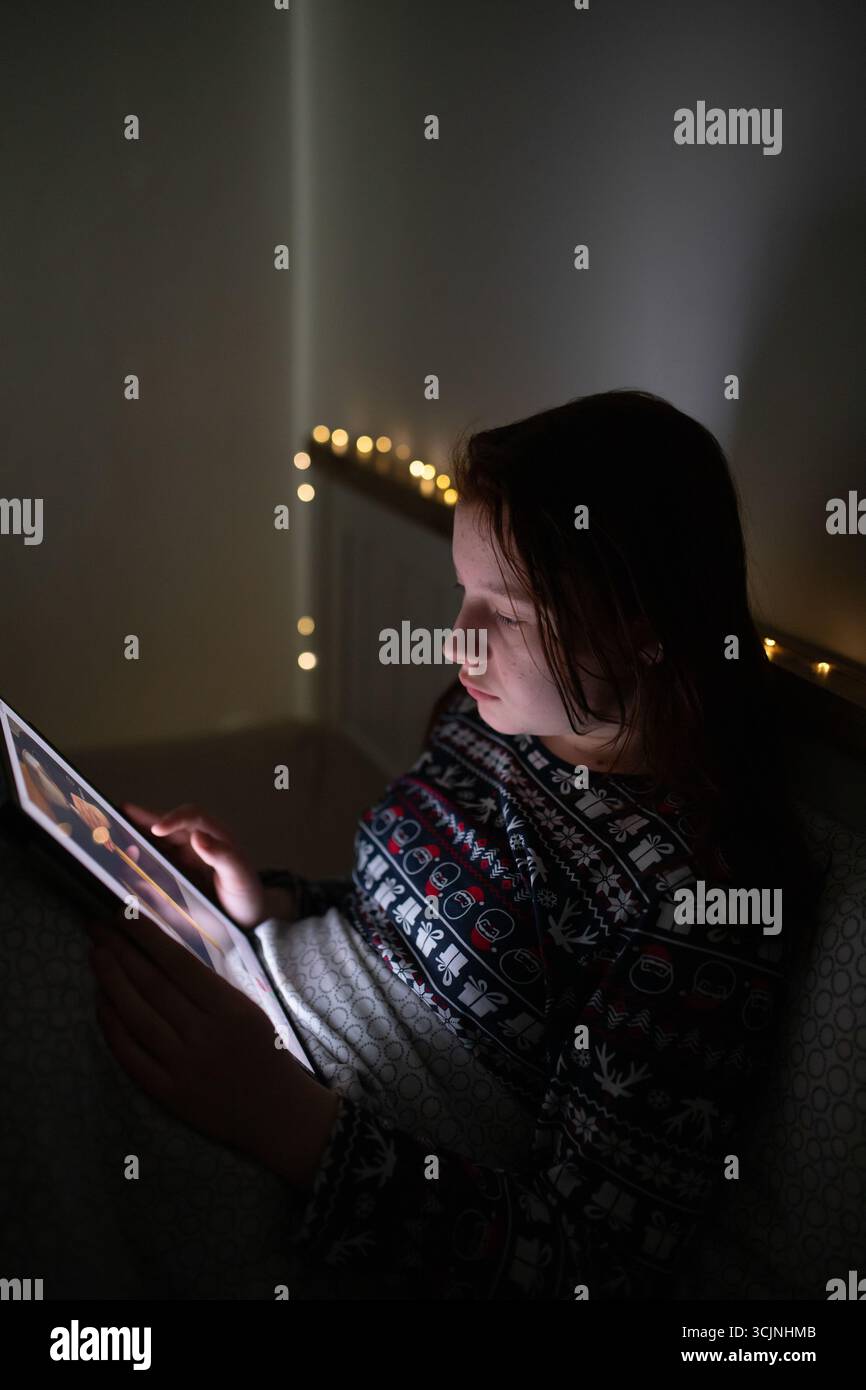 Ragazza adolescente che usa lo smartphone, tablet sdraiata a letto a tarda notte. Concetto di dipendenza dallo schermo per bambini. Foto Stock