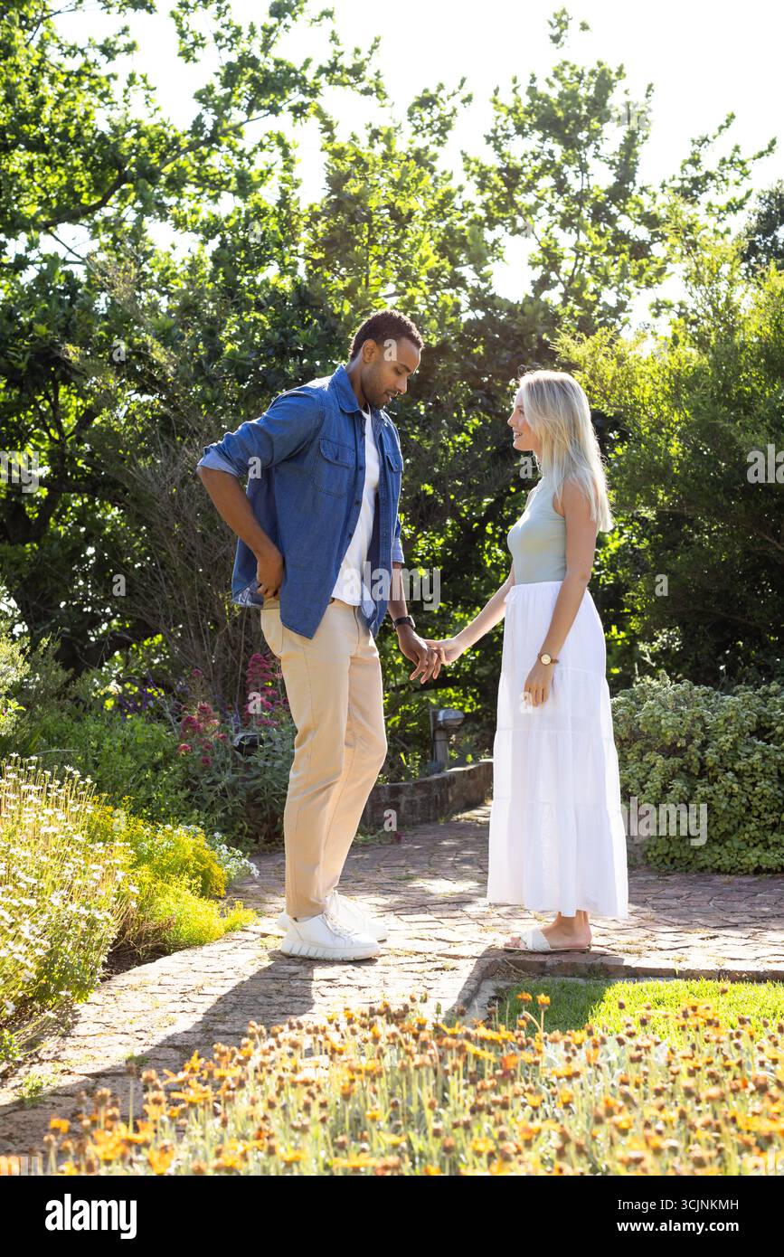 Coppia che si tiene per mano in un giardino soleggiato, godendosi momenti romantici insieme Foto Stock