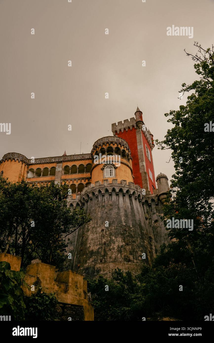 Vista dal basso del Palácio da pena a Sintra, Portogallo, che mostra le sue mura grigie simili a una fortezza, la torretta gialla e la torre rossa. Foto Stock