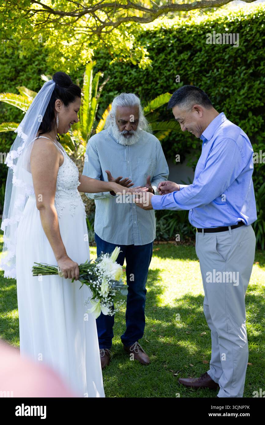 Scambio di anelli, sposa e sposo nella cerimonia del giardino con officiante presente Foto Stock