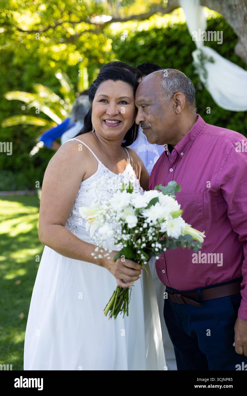 Celebrazione di un matrimonio senior all'aperto, coppia senior sorridente con donna che tiene un bouquet di fiori bianchi Foto Stock