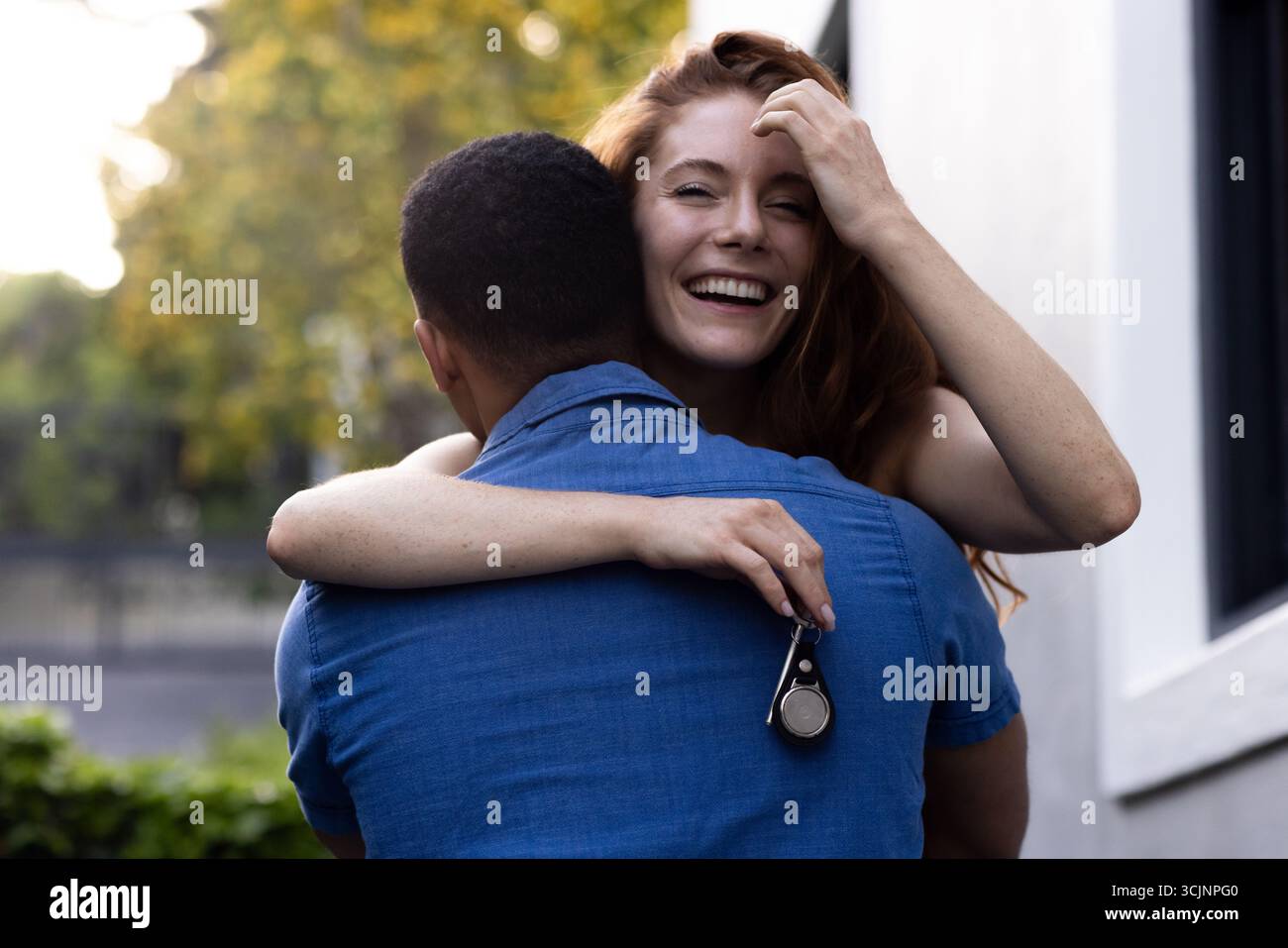 Una giovane coppia che abbraccia l'aria aperta, una donna sorride gioiosamente mentre tiene le chiavi in mano Foto Stock