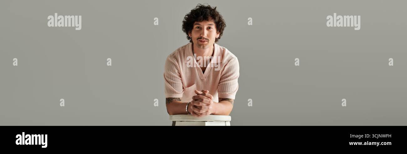 Un bel giovane uomo poggia elegantemente su uno sfondo semplice, trasudando stile e stile disinvolto. Foto Stock