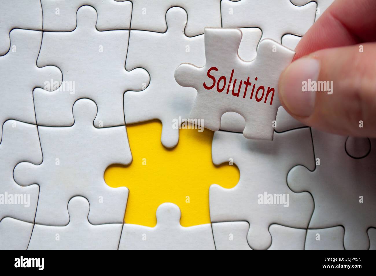 Soluzioni, mano umana posizionare un pezzo di puzzle etichettato soluzioni in un puzzle quasi completo con altri termini di leadership visibili Foto Stock