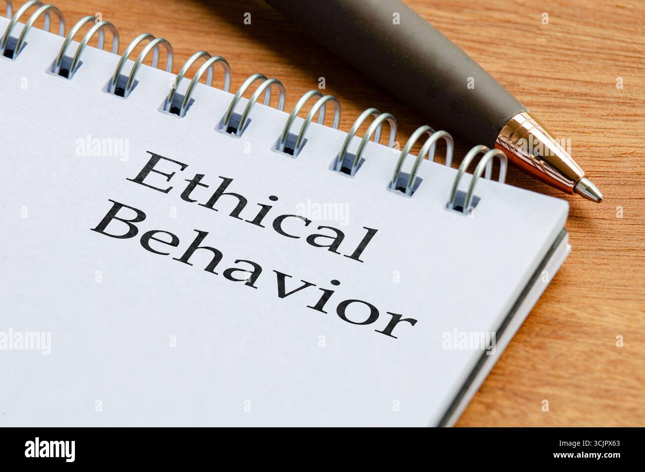 Primo piano del blocco note con le parole "comportamento etico" scritte su una pagina posta su una scrivania di legno con accanto una matita Foto Stock