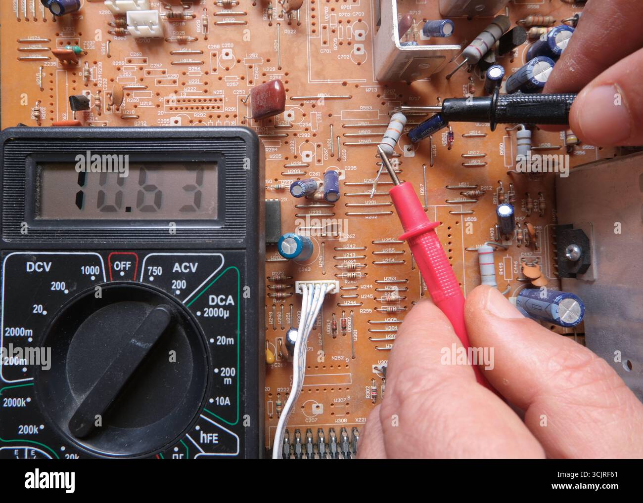 Test di un componente elettronico con il multimetro. Un resistore elettrico è sottoposto a test da parte di personale tecnico sulla scheda a circuito stampato. Foto Stock