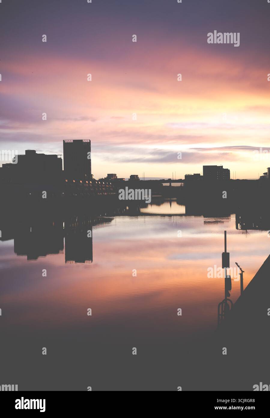 Tramonto colorato sullo skyline della città di Glasgow che si riflette sull'acqua del fiume Clyde con edifici sagomati e il suggestivo cielo che crea un paesaggio urbano panoramico Foto Stock