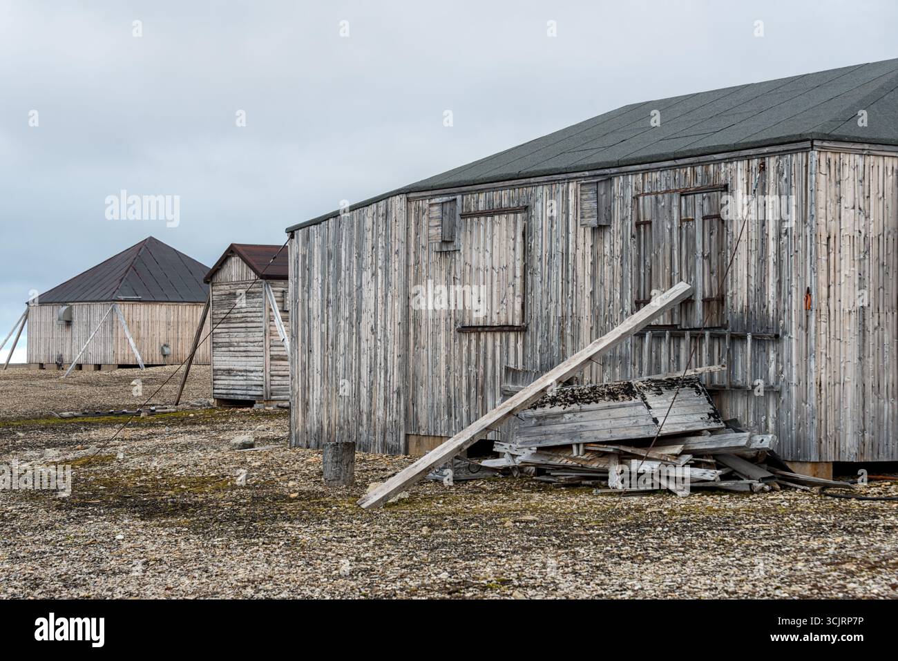 Stazione di Kinnvika Nordaustlandet Svalbard Norvegia // NORDEAUSTLANDET, Svalbard — le strutture in legno intemperie della stazione di Kinnvika, fondata nel 1957 nell'ambito dell'anno geofisico internazionale, si trovano sul paesaggio arido di Nordaustlandet, Svalbard. Questa remota stazione di ricerca artica è servita come base per spedizioni scientifiche ed è una testimonianza degli sforzi passati nella ricerca polare. Gli edifici abbandonati della stazione e il terreno ghiaioso circostante evidenziano le dure condizioni ambientali della regione. Foto Stock