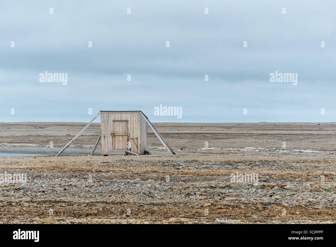 Kinnvika Station Research Hut Nordaustlandet Svalbard Norvegia // NORDEAUSTLANDET, Svalbard — Una capanna di ricerca in legno, identificata come stazione Kinnvika, si erge su un paesaggio roccioso e arido sotto un cielo coperto. La stazione si trova a Nordaustlandet, una grande isola dell'arcipelago delle Svalbard in Norvegia. La stazione di Kinnvika, fondata nel 1957 come parte dell'anno geofisico internazionale, è stata un importante centro per la ricerca scientifica artica e la cooperazione internazionale. La sua posizione remota nella parte nord-orientale del Nordaustlandet, caratterizzata da tundra e caratteristiche glaciali, ha fornito un'esperienza unica Foto Stock