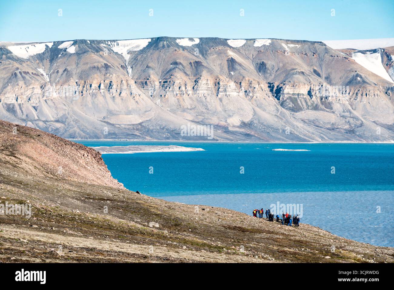 Faksevagen Svalbard paesaggio artico con turisti Spitsbergen // SPITSBERGEN, Svalbard - Un gruppo di turisti osserva il paesaggio artico di Spitsbergen, un'isola nell'arcipelago delle Svalbard. L'immagine cattura il terreno accidentato dell'isola, con pendii rocciosi che scendono verso le limpide acque blu dell'Oceano Artico. Sullo sfondo, si innalzano maestose montagne, le cui vette sono ricoperte di neve e ghiaccio, mostrando le drammatiche formazioni geologiche della regione. Le Svalbard sono note per il loro ambiente polare unico, caratterizzato da ghiacciai, fiordi e una varietà diversificata di fauna selvatica artica. L'ar Foto Stock