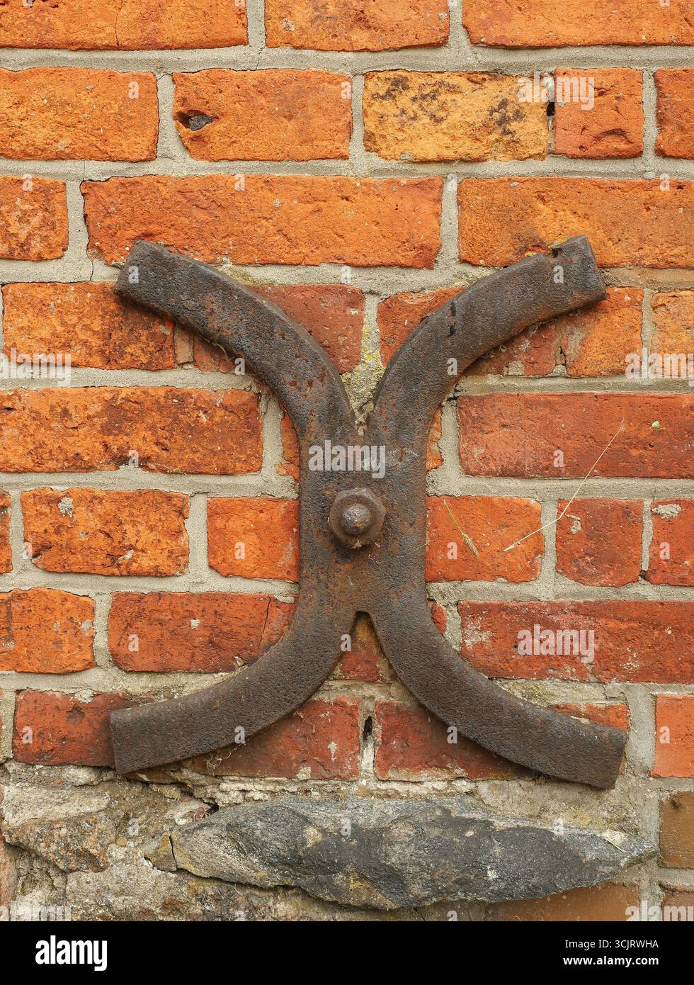 Piastra di ancoraggio forgiata in ferro a forma di croce curva, fissata alla base di una vecchia facciata. Copyspace Foto Stock