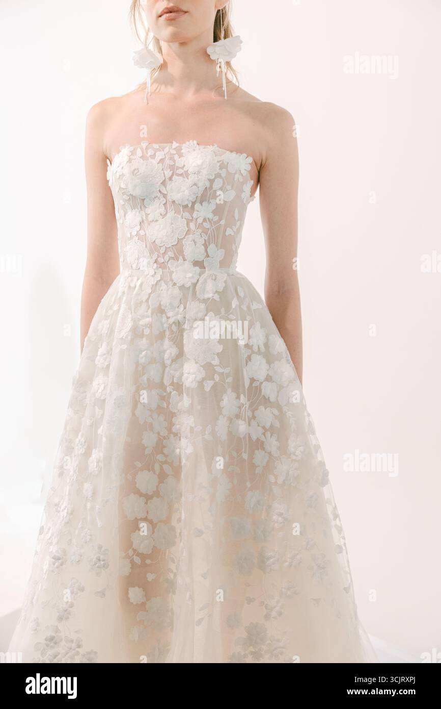 Modello che indossa un abito da sposa senza spalline con intricati dettagli floreali in pizzo, per un'eleganza in uno studio luminoso. Foto Stock