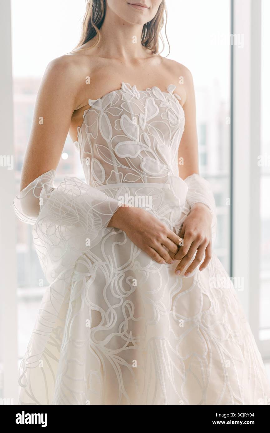 Un modello sfoggia uno splendido abito da sposa senza spalline con motivi floreali e dettagli trasparenti in un ambiente contemporaneo. Foto Stock