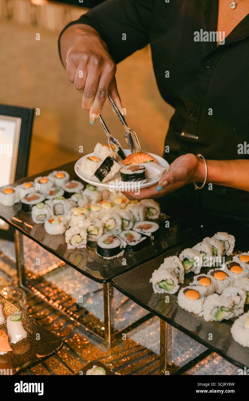 Un abile chef serve una variegata gamma di sushi roll in un incontro sociale, mettendo in risalto l'arte della preparazione del sushi. Foto Stock