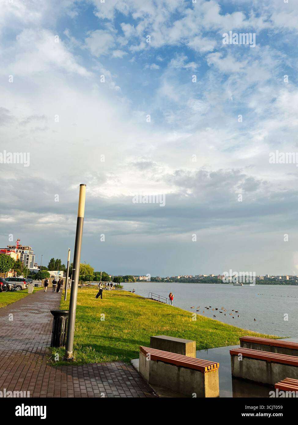 Tarnopil, Ucraina - 10 agosto 2025: Tranquilla passerella lakerside con erba verde, panchine e vista sulla città. Foto Stock