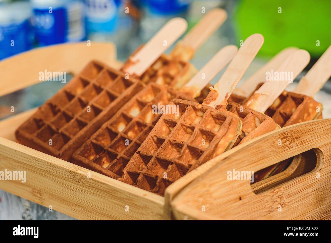 Waffle dorati croccanti serviti su bastoncini di legno, disposti ordinatamente in un vassoio di bambù Un tocco creativo e portatile per un dolce classico Foto Stock