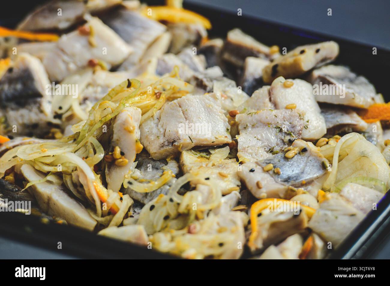 Primo piano di un piatto saporito con pezzi di aringhe cotti mescolati con cipolle saltate, carote e spezie Foto Stock