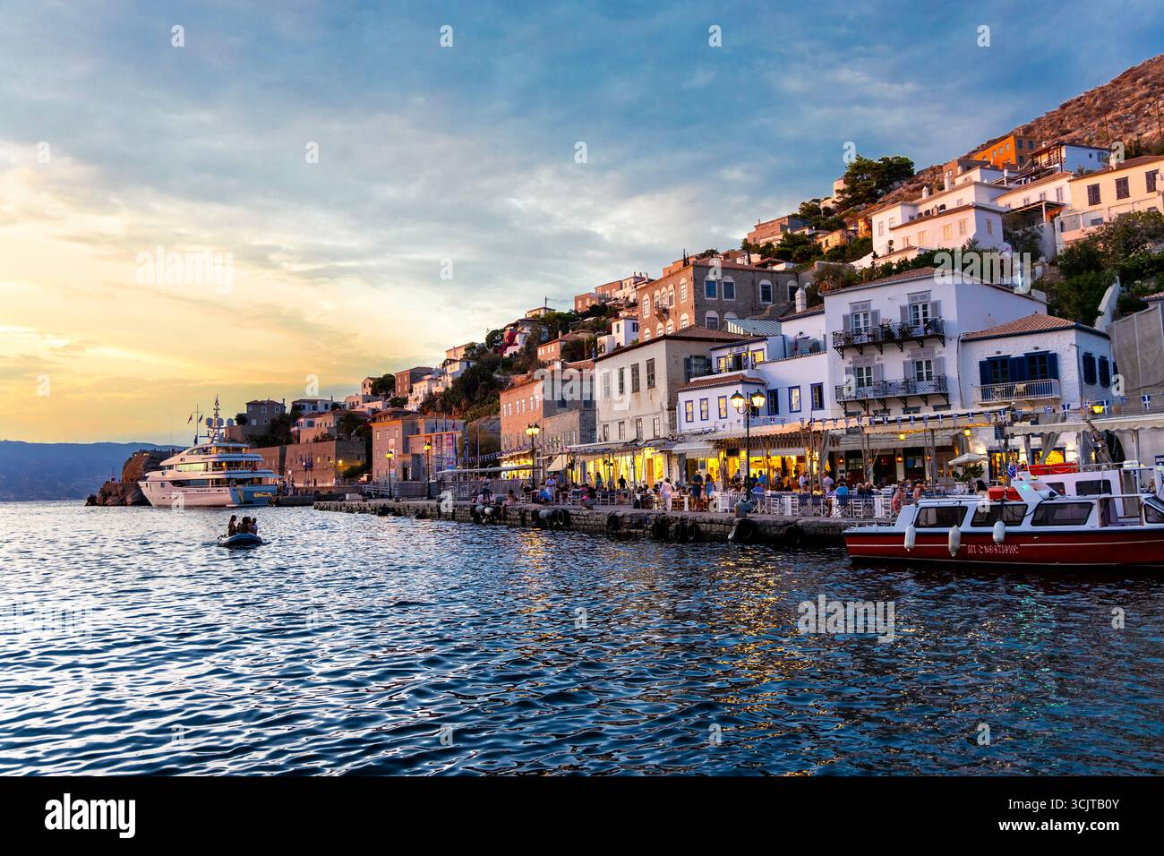 Ristoranti lungo il lungomare al tramonto a Hydra Town, Hydra Island, Saronic Islands, Grecia Foto Stock