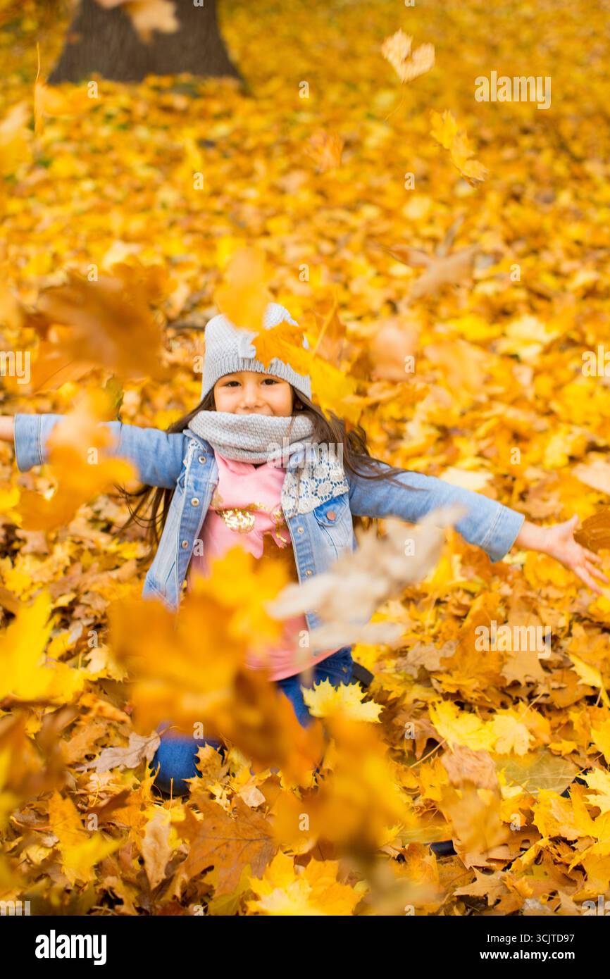 ragazza felice che lancia le foglie autunnali in aria con piena di gioia di vivere Foto Stock