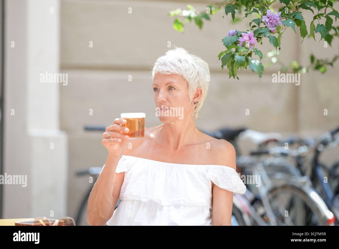 Una donna è seduta a un tavolo con un bicchiere di birra davanti a lei. Indossa una camicia bianca e i capelli vengono tirati indietro. La scena e' ambientata in una p Foto Stock