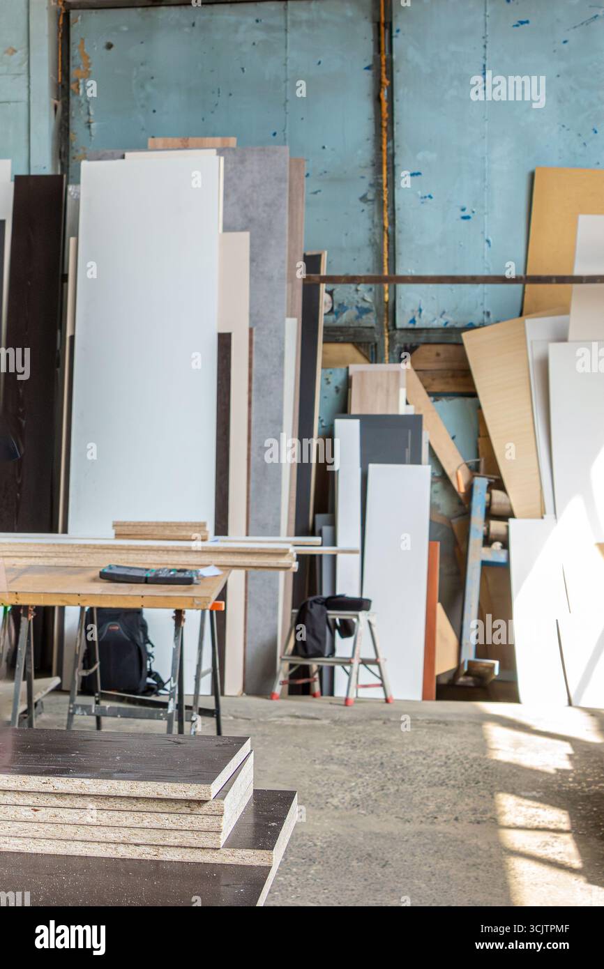 Un'officina accogliente ma impegnata con alte pile di pannelli in legno e pezzi rimanenti, tutto pronto per il prossimo progetto, con una messa a fuoco selettiva Foto Stock