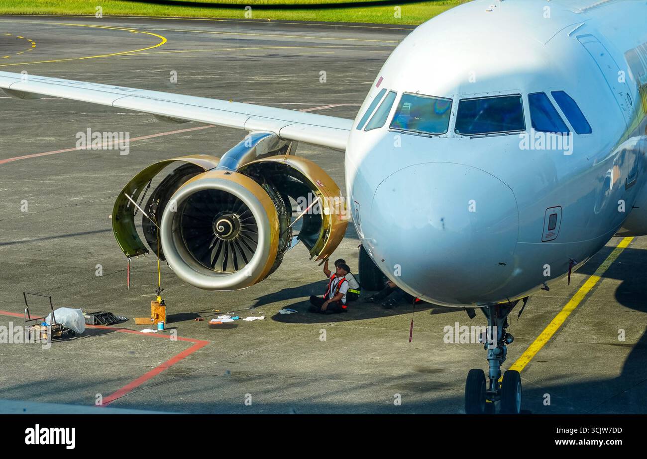 Il meccanico dell'aeroplano sta lavorando su un motore dell'aeromobile sull'asfalto, che serve il jet all'esterno; ideale per i progetti di viaggio o di settore dell'aviazione. Foto Stock
